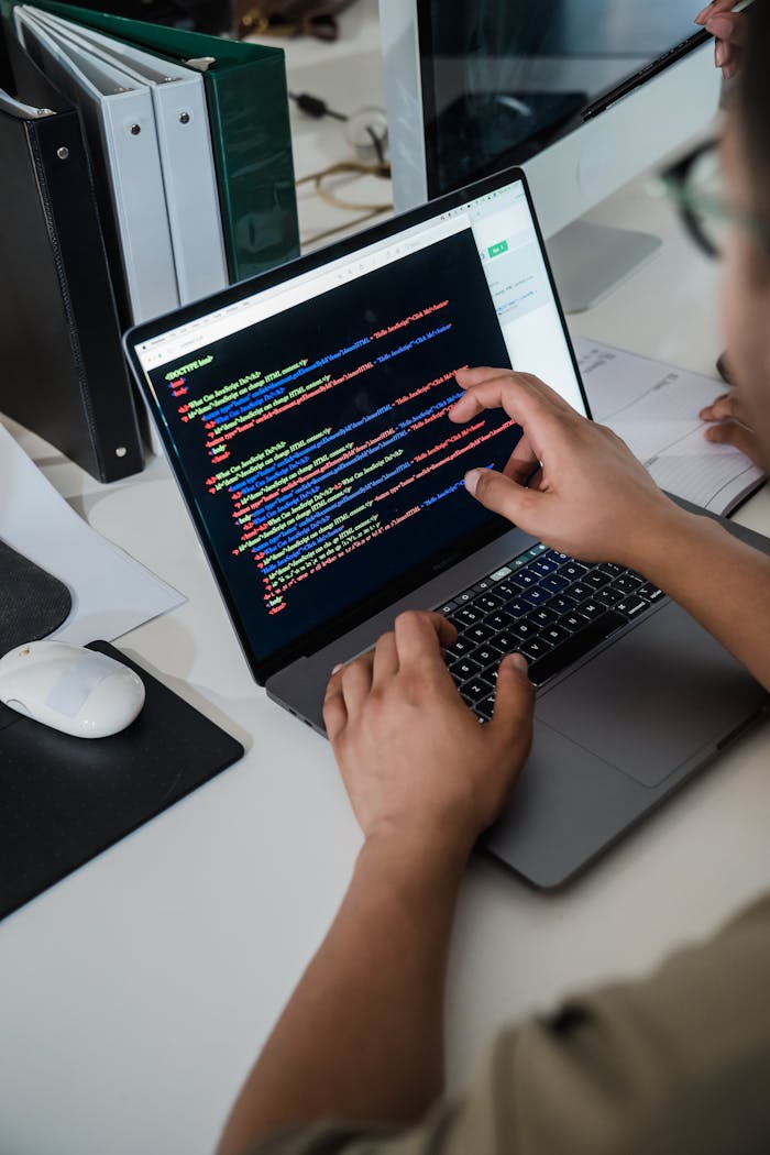 Home Close-up of a programmer pointing at a colorful code script on a laptop in an office setting.