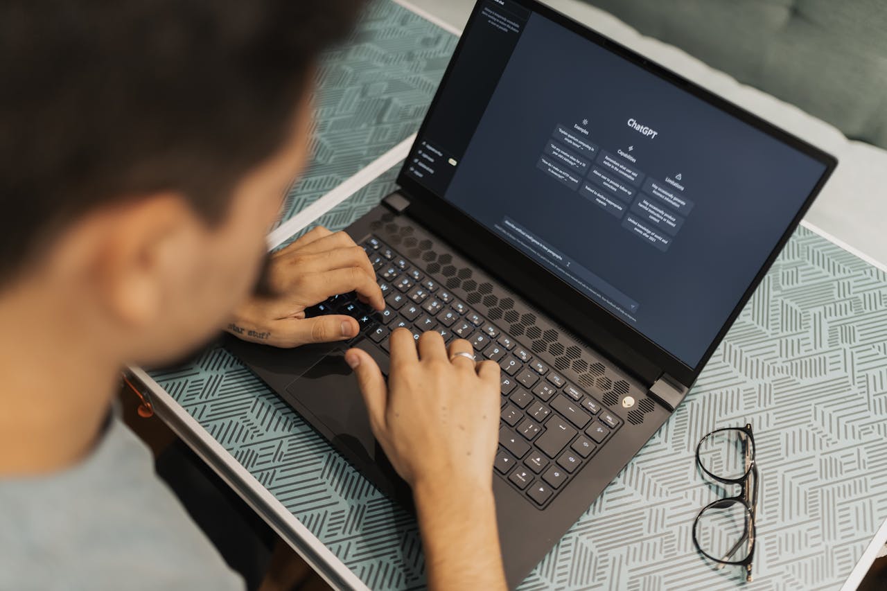 Services A man working on a laptop with AI software open on the screen, wearing eyeglasses.