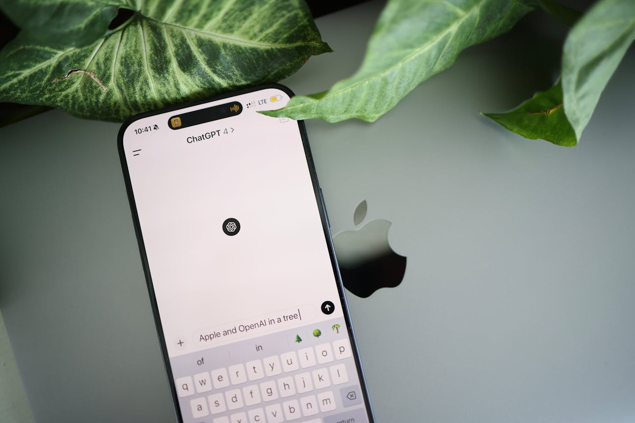 About A smartphone shows a ChatGPT interface placed on an Apple laptop in a leafy environment.